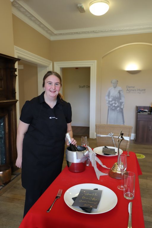 Supported intern Maisy stands next to a restaurant table that she has laid out for a table-laying competition.