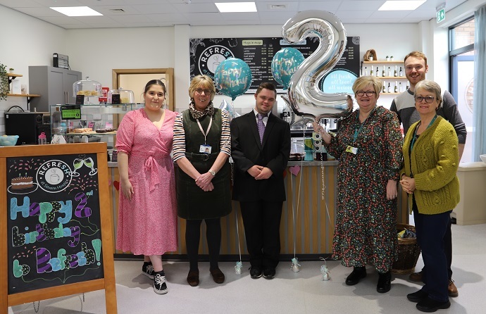 The Refresh Cafe team, including Derwen student George Weston - wearing a suit - stand in front of the Refresh counter with birthday balloons.