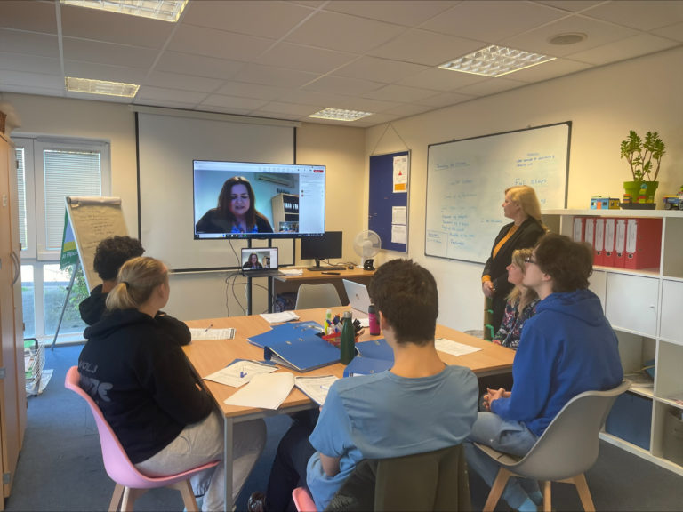 Ludlow students sit around a classroom table watching a big screen with functional skills teacher Leah announcing competition winners.